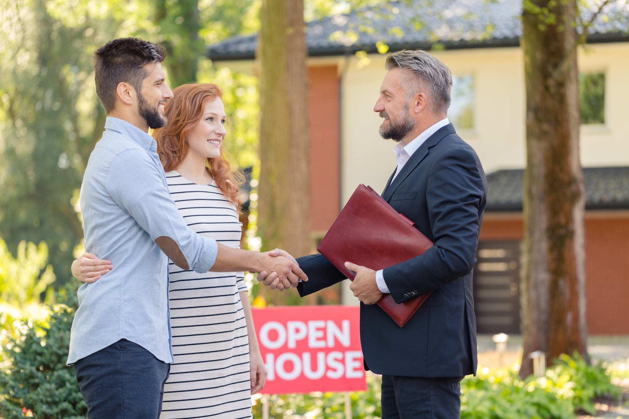 Real estate agent welcoming young smiling couple and inviting to presentation of house